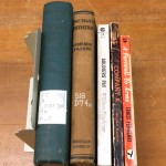 Spines of five novels, left to right, largest to smallest: Through the Wheat (dark blue), On Man's Initiation (camel brown), Soldiers' Pay (white), Company K (black), A Farewell to Arms (orange)