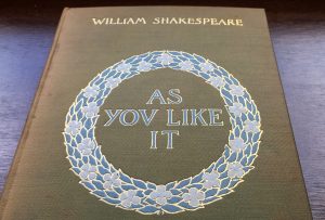 Cover of 1900 version of Shakespeare's As You Like It, with title inside embossed floral ring, in blue, white, and gold, using the old spelling of the letter V for the letter U